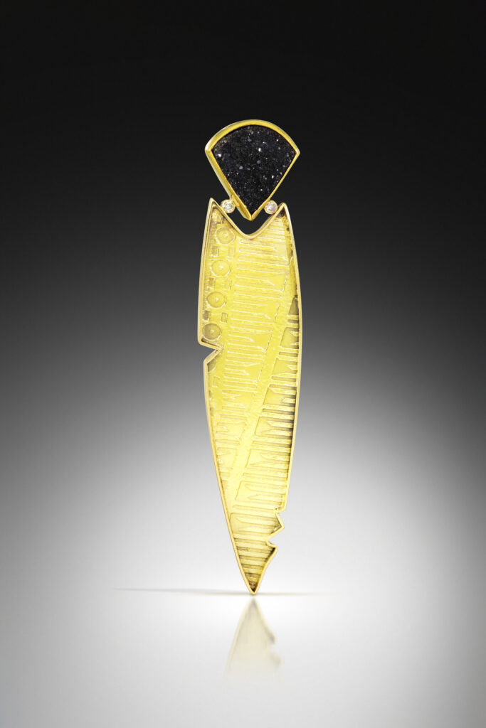 Picture of a brooch made by Barbara McFadyen, entitled the Feather of Truth (Ma'at Feather). The brooch is a mixture of materials and features an embossed gold metal with black druzy quartz and diamonds as accents. 